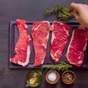 raw new york strip steaks wood cutting board